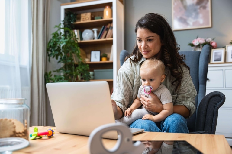 a woman holding a baby while looking at a laptop