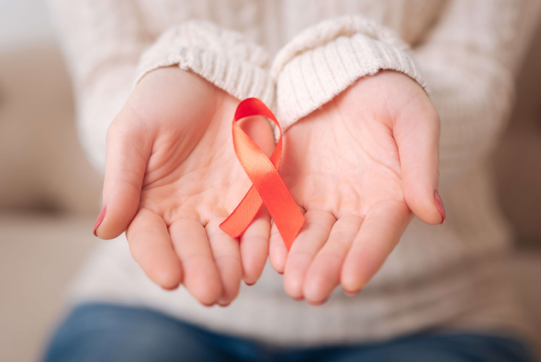 Person holding a red ribbon in their hands as a symbol of HIV/AIDS awareness.